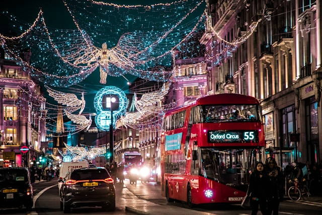 Busy city street with double-decker bus and festive lights at night.