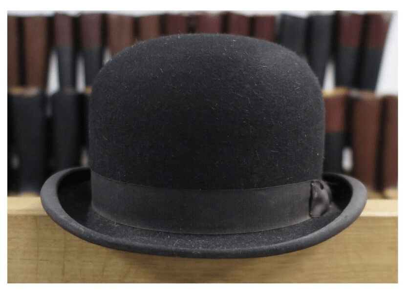 A black bowler hat on a wooden surface with dark books behind.