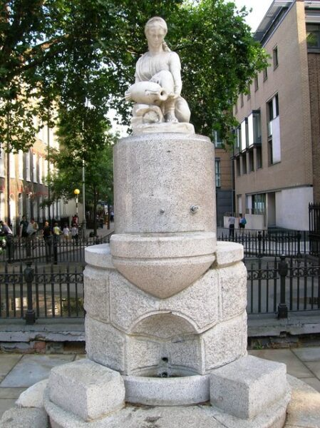 Statue of a woman with jug atop a stone fountain outdoors.