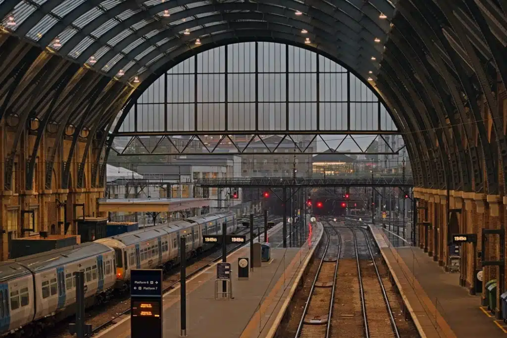 Train station with arched roof, tracks, and waiting trains at dusk.