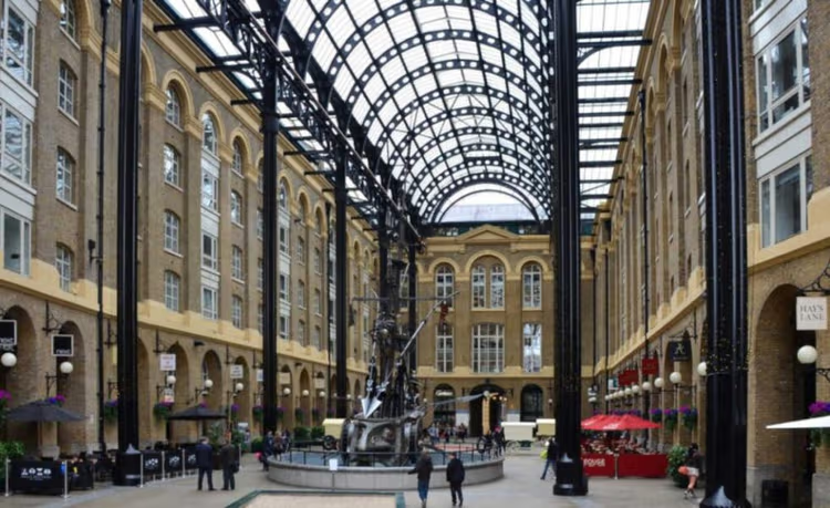 Covered atrium with glass roof, arched steel beams, and people walking around.