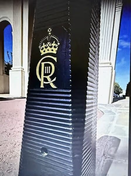 Black post with a gold crown and 'C III R' emblem outside a building.