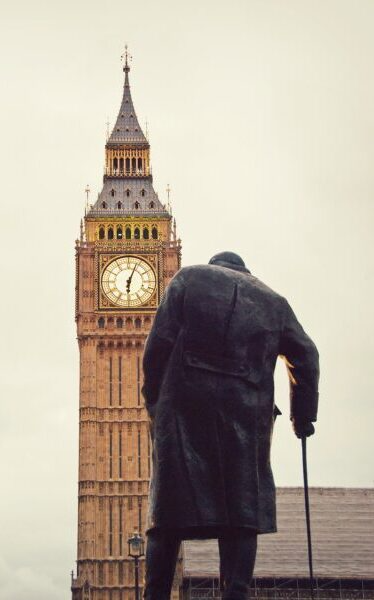 Statue of a man with cane facing Big Ben clock tower.