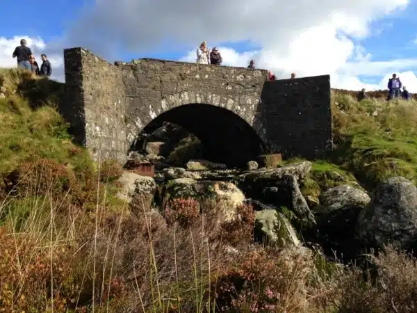 Stone bridge over a stream with people standing and walking near it.