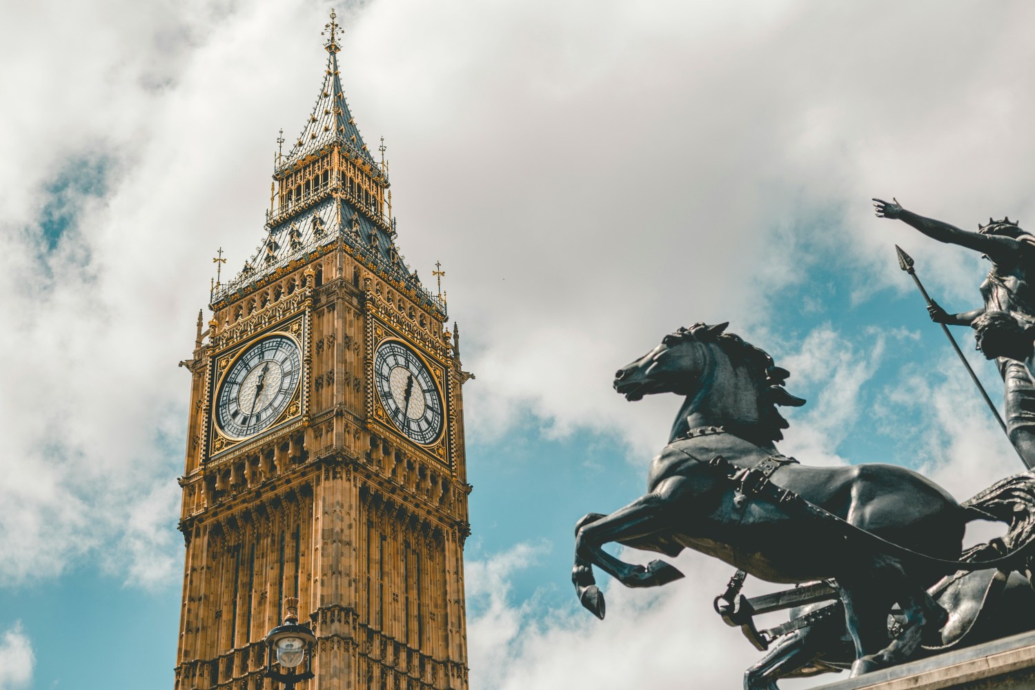 Big Ben tower against cloudy sky with statue of horse and rider in foreground.