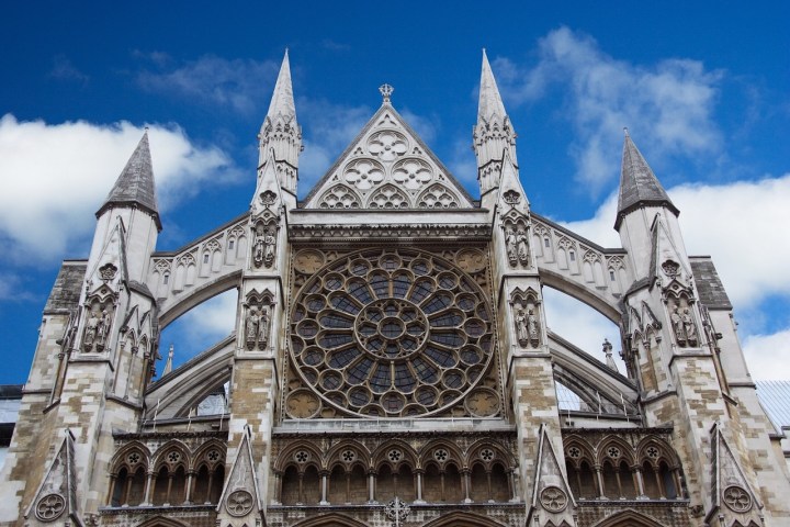 Gothic cathedral facade with a large circular window and pointed arches under a blue sky.