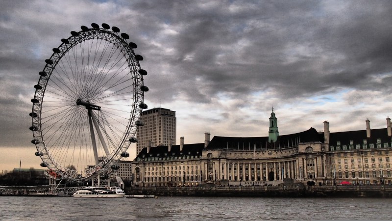 Ferris wheel near a historic building by the river under a cloudy sky.