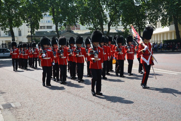 Soldiers in red uniforms and bearskin hats marching with instruments on a street.