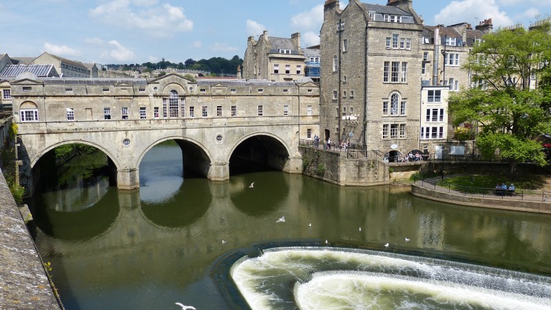 Historic stone bridge over a river with adjacent buildings and a waterfall.