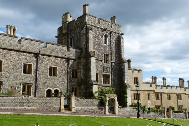 Historic stone castle with towers and green lawn under a cloudy sky.
