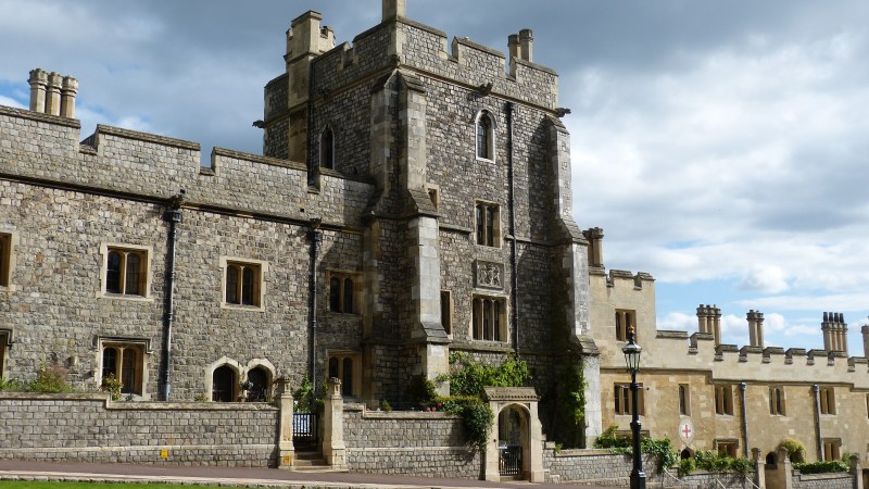 Historic stone castle with towers and green lawn under a cloudy sky.