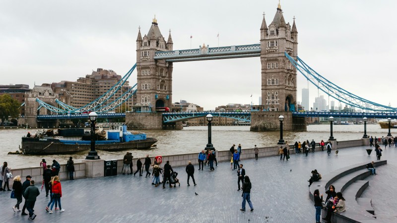 People walking near Tower Bridge over River Thames on a cloudy day.