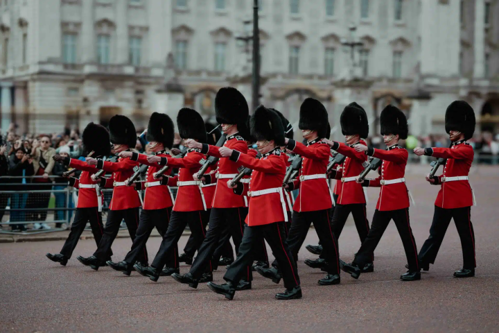 Soldiers in red uniforms and bearskin hats marching in formation.