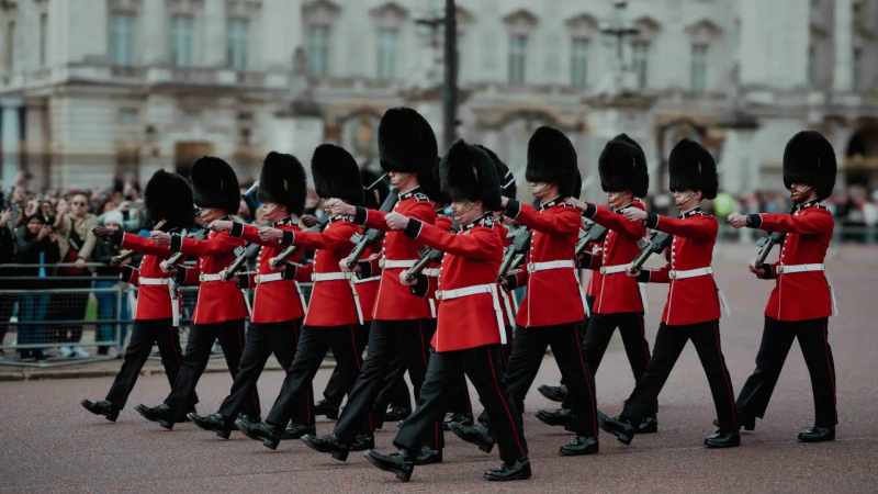 Soldiers in red uniforms and bearskin hats marching in formation.