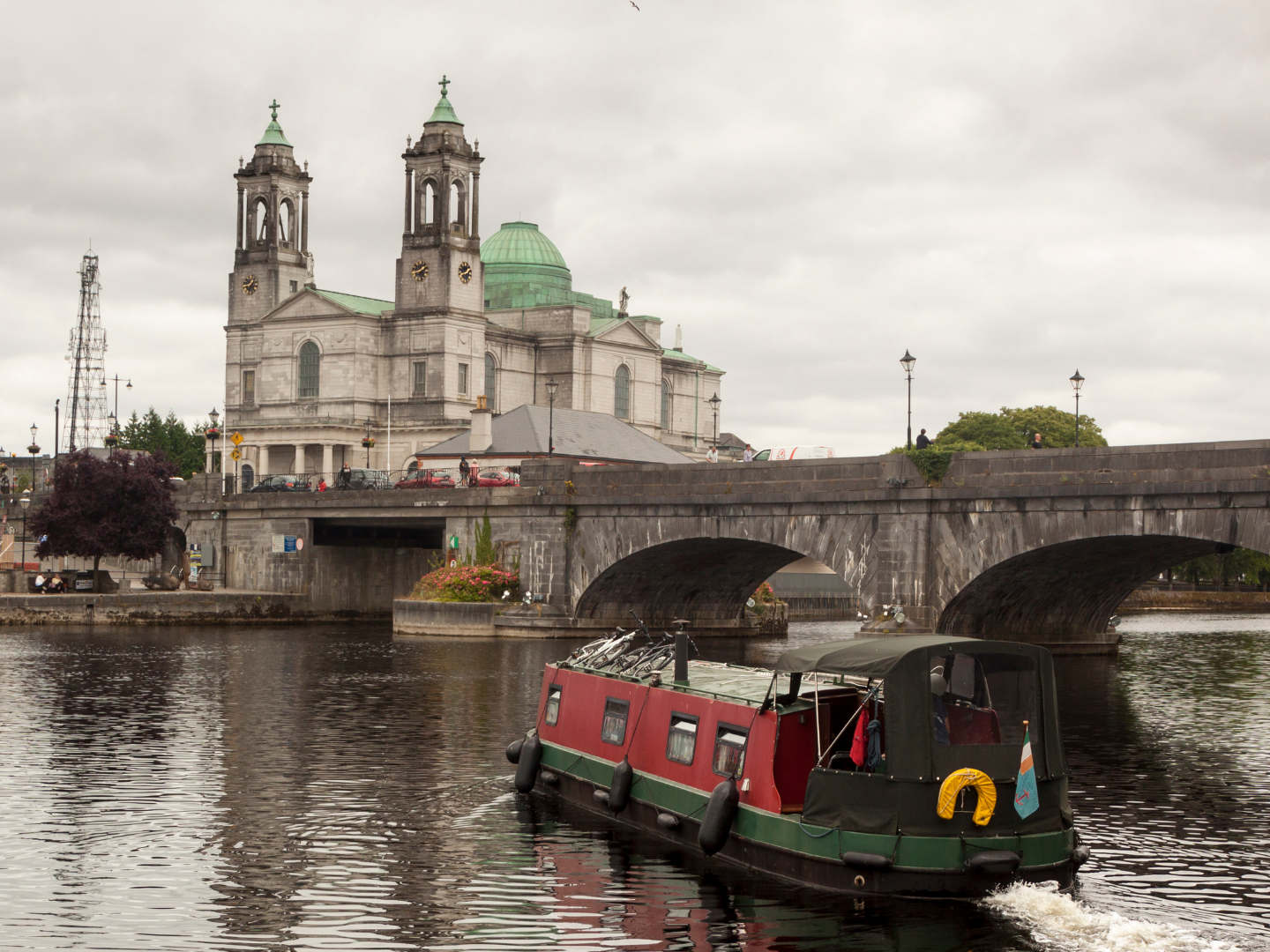 Boat on river with stone bridge and cathedral in the background.