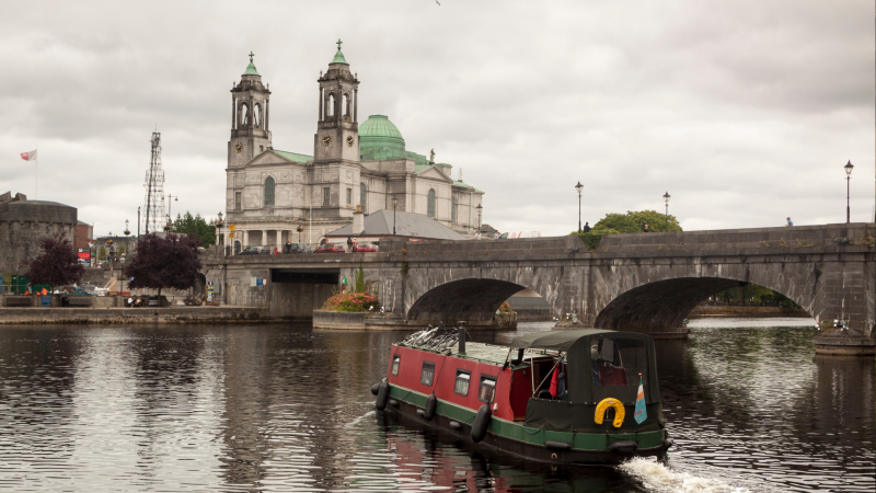 Boat on river with stone bridge and cathedral in the background.