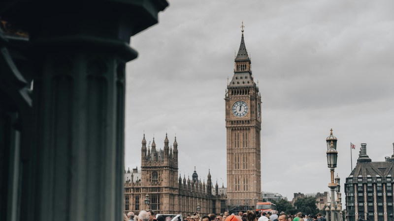 People on a bridge with Big Ben in the background under cloudy skies.
