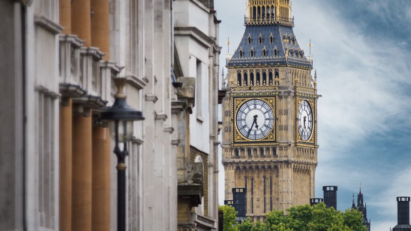 View of Big Ben clock tower framed by buildings and trees under a cloudy sky.