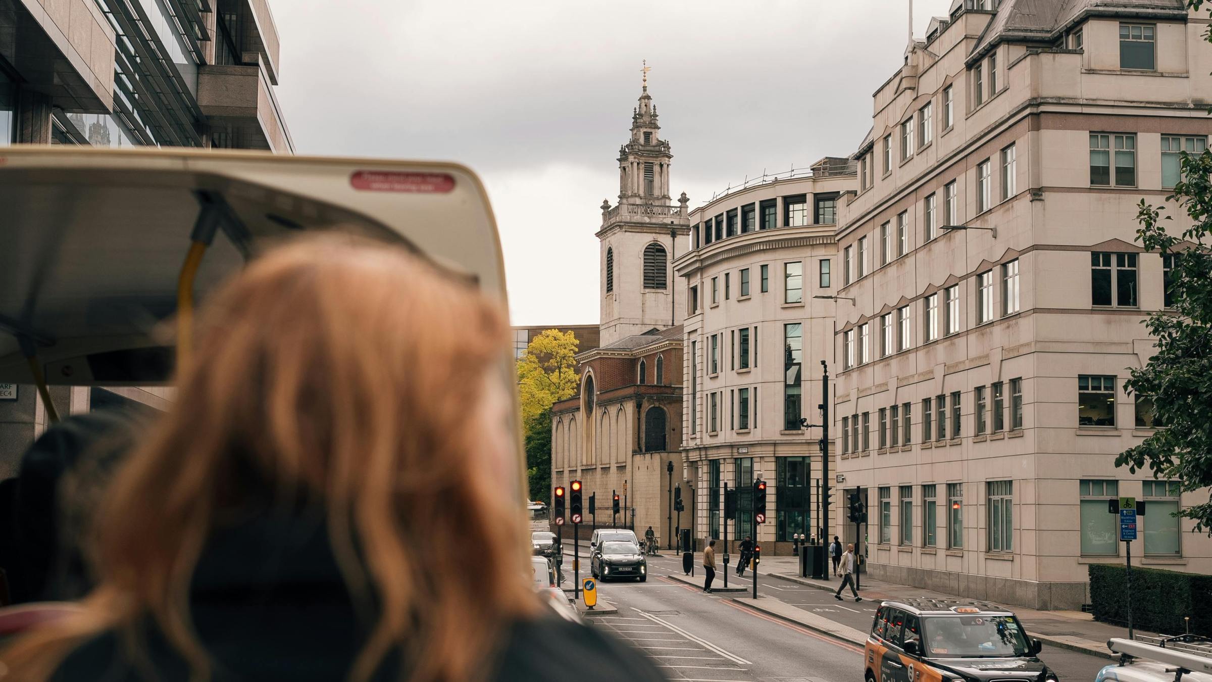 Person on double-decker bus viewing city street with historic building.