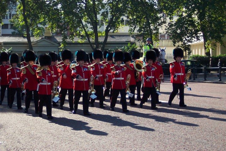Marching band in red uniforms with black hats performing outdoors.
