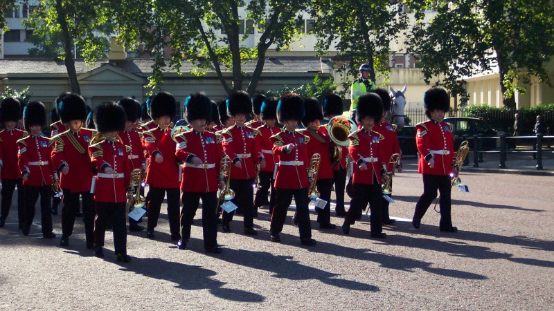 Marching band in red uniforms with black hats performing outdoors.