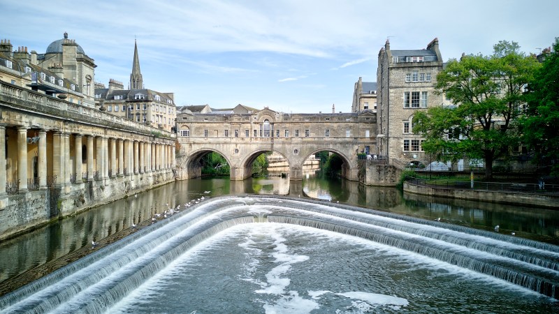 Historic stone bridge and buildings over a river with cascading water.