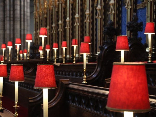 Row of red lamps in a church with intricate wood and metalwork.