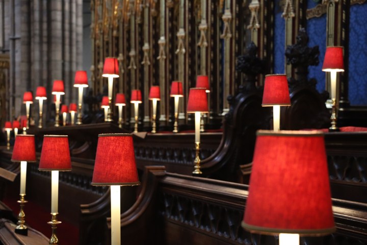 Row of red lamps in a church with intricate wood and metalwork.
