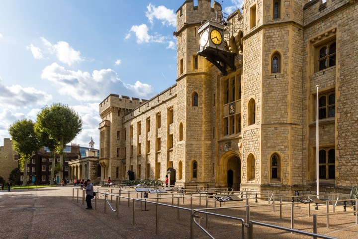 Historic stone castle with clock tower, blue sky background.