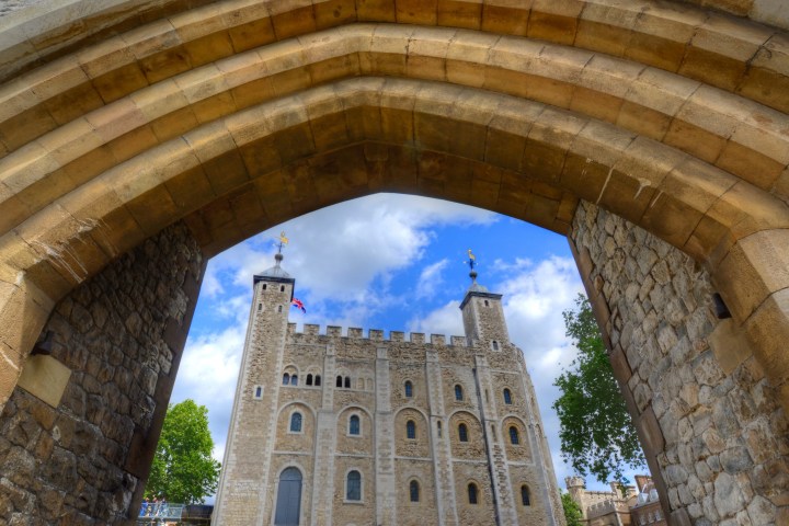 View of a historic castle through a stone archway under a blue sky.