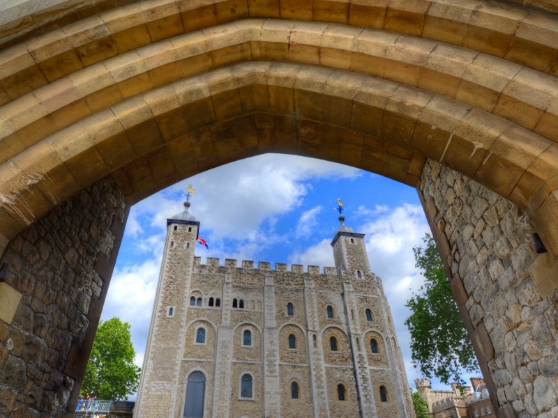 View of a historic castle through a stone archway under a blue sky.